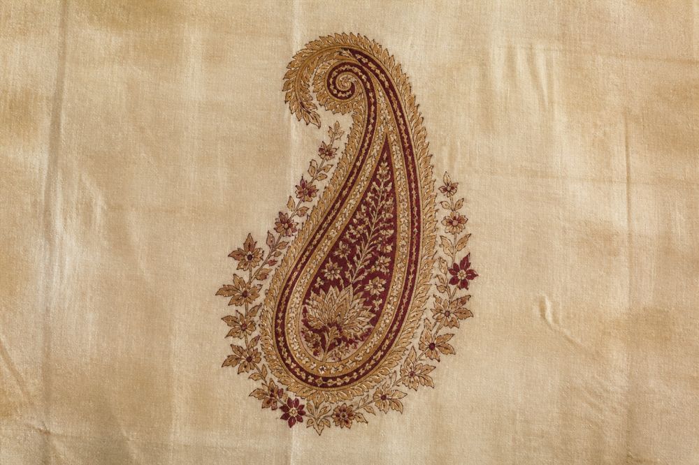 A single gold and maroon paisley buta, block printed on cream cloth.